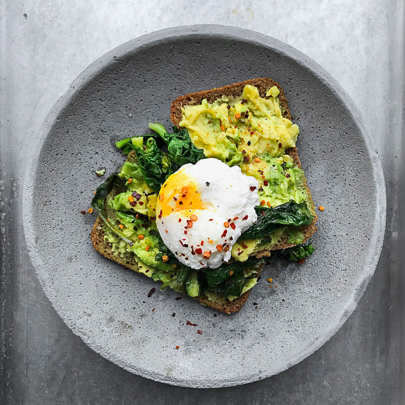 Avocado-Toast mit pochiertem Ei auf grauem Teller