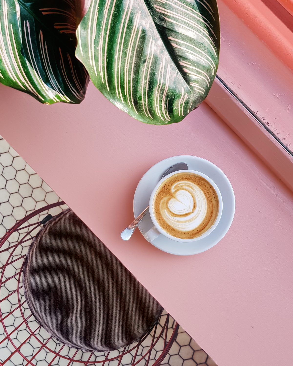 Flat White auf einem rosafarbenen Marmortisch mit Pflanzenschatten