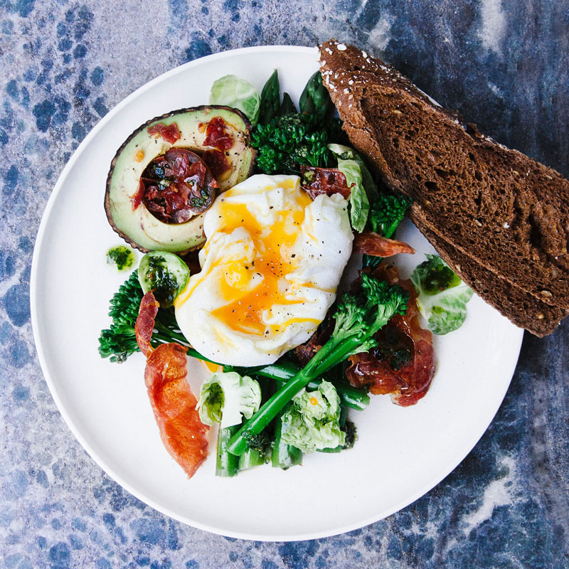 Frühstücksteller mit pochiertem Ei und Avocado auf einem Marmortisch im Cey'se Café